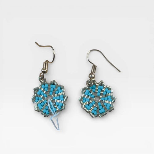 Aretes Huichol de chaquira azul turquesa y plata con patrón geométrico.
