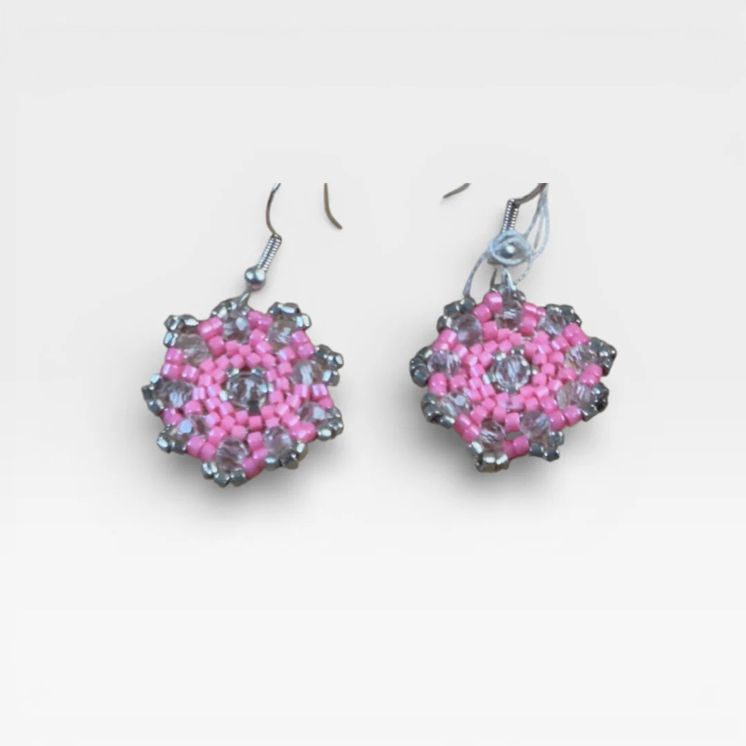 Aretes Huichol de chaquira, rosa y gris cristalino, con patrón floral geométrico.
