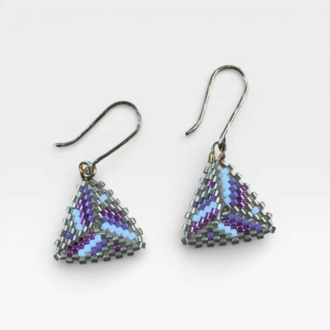 Aretes Wixárika de chaquira, patrón geométrico triangular morado, azul cielo y gris.