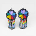 Aretes de chaquira negros, flor Huichol multicolor y flecos vibrantes.