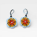 Aretes de chaquira Wixárika con patrón floral en naranja, amarillo y azul celeste.