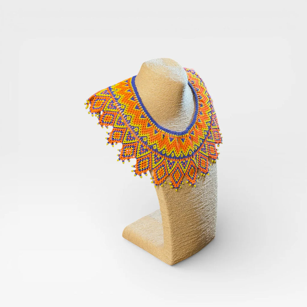 Collar Huichol de chaquira naranja, amarillo y azul con patrón de rombos geométricos.