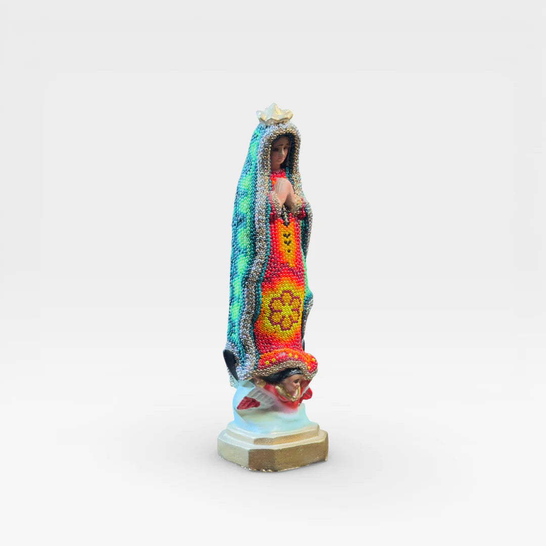 Figura de Chaquira Huichol: Virgen de Guadalupe verde, roja y amarilla con símbolo floral.