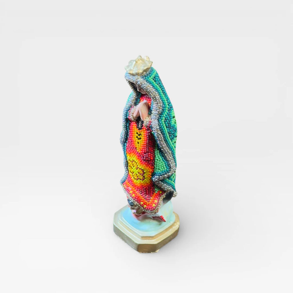 Figura de Chaquira Huichol: Virgen de Guadalupe verde, roja y amarilla con símbolo floral.